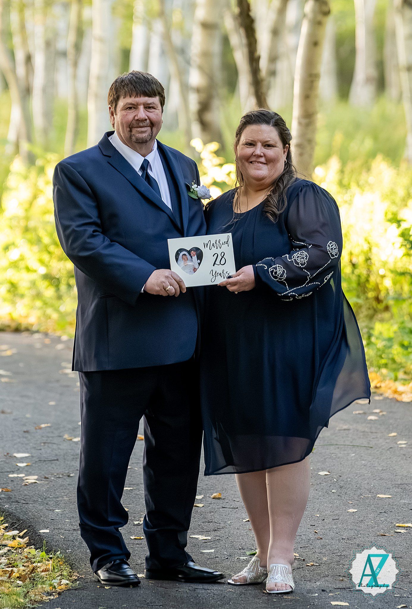 Wedding couple shares a playful moment holding signs in a wooded outdoor setting.