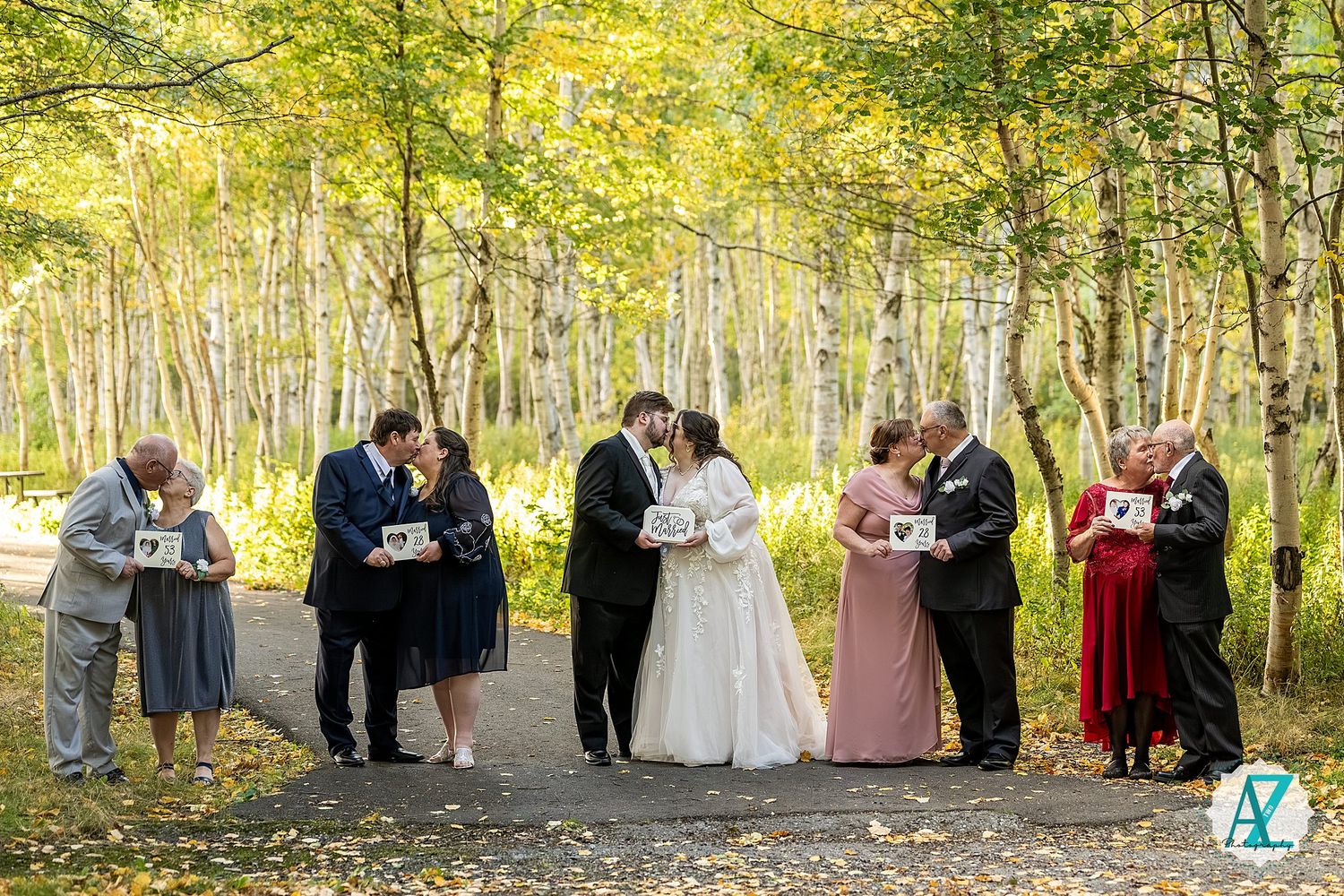 Wedding group photo with bridal party standing in line among autumn birch trees with golden foliage.