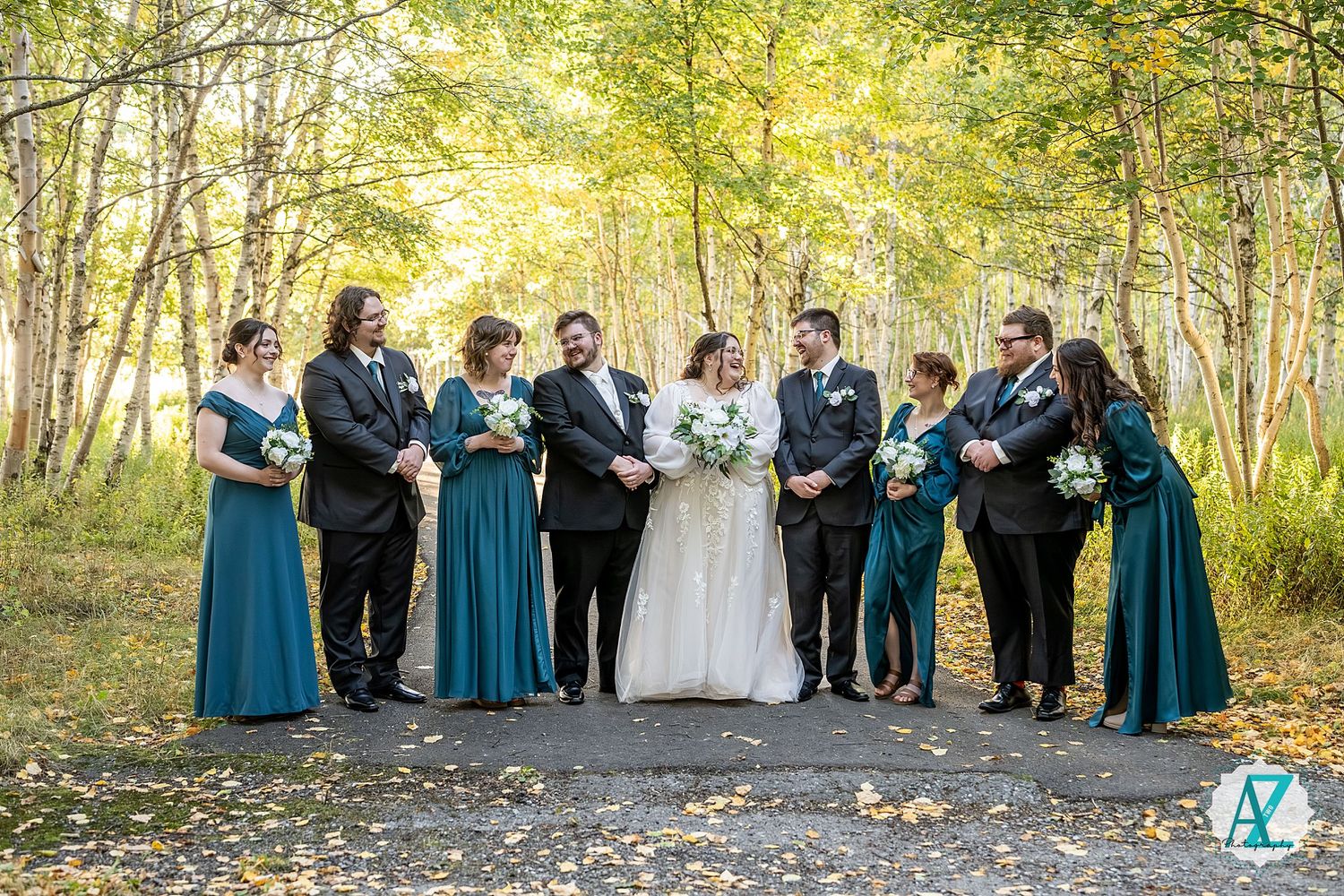 Wedding party lined up for formal photos in a sunlit birch forest with teal bridesmaid dresses.