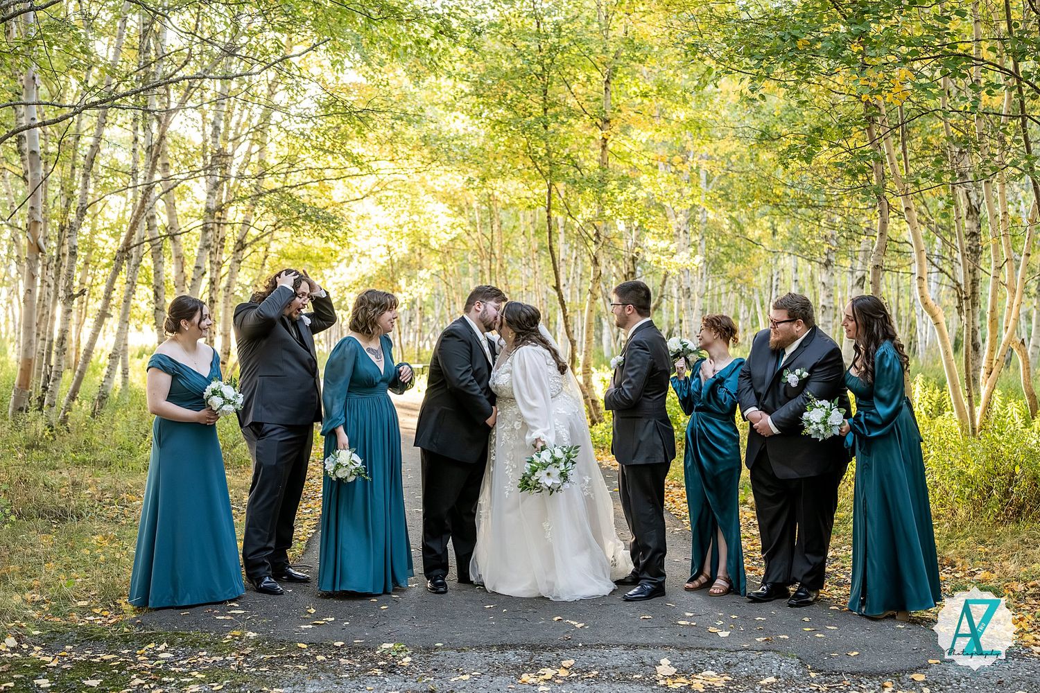 Wedding ceremony group photo with bridesmaids in teal dresses surrounded by autumn trees.