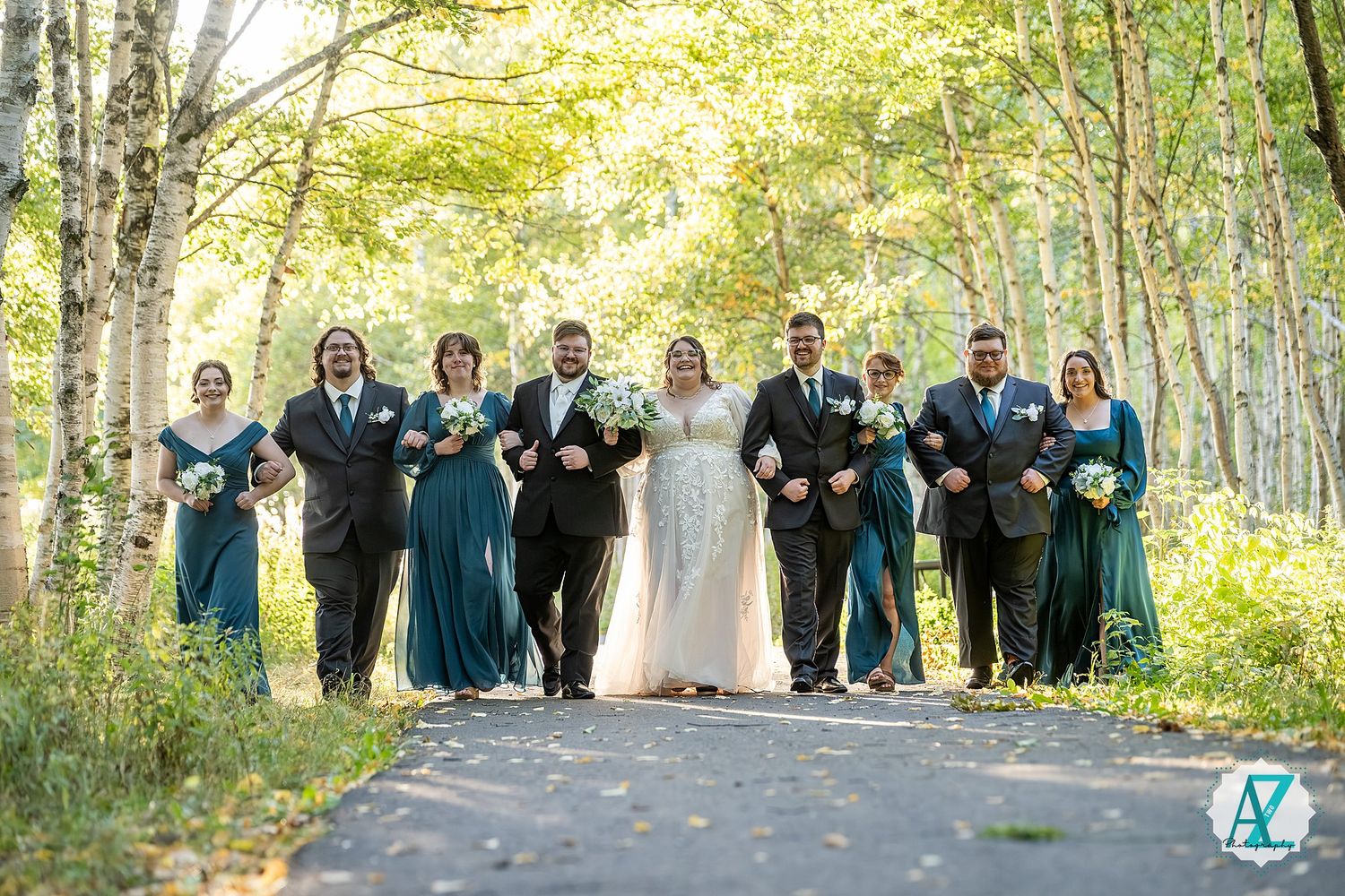 Large wedding party gathered in a sunlit birch forest for group photos during fall season.