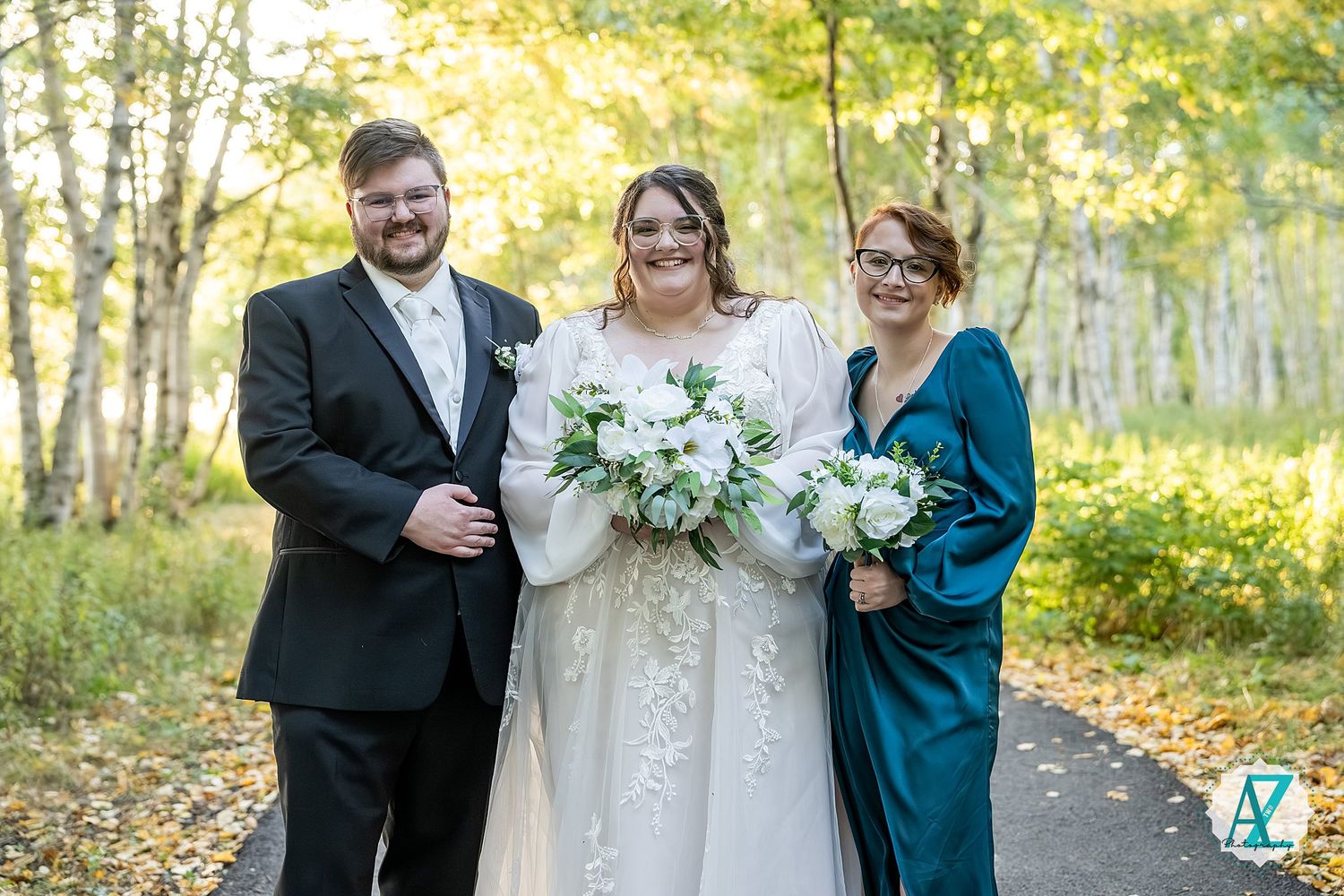 Wedding party celebrates outdoors among birch trees with bridesmaids in teal dresses.