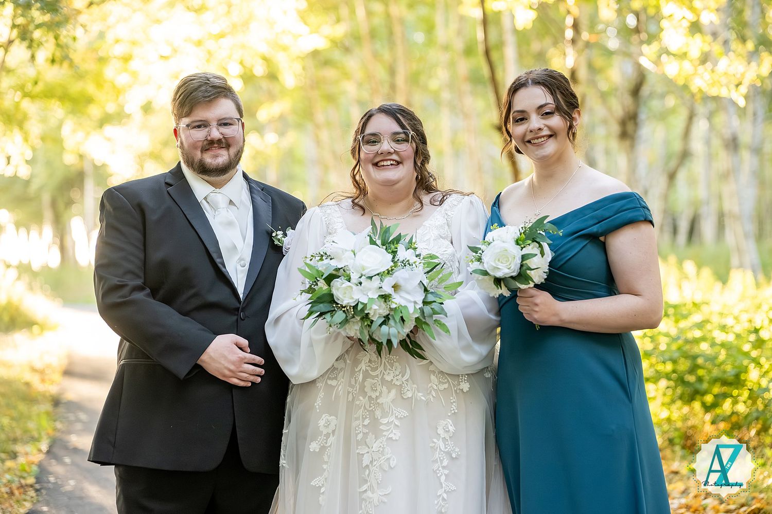 Wedding party members pose together in a sunlit birch forest with white floral bouquets.