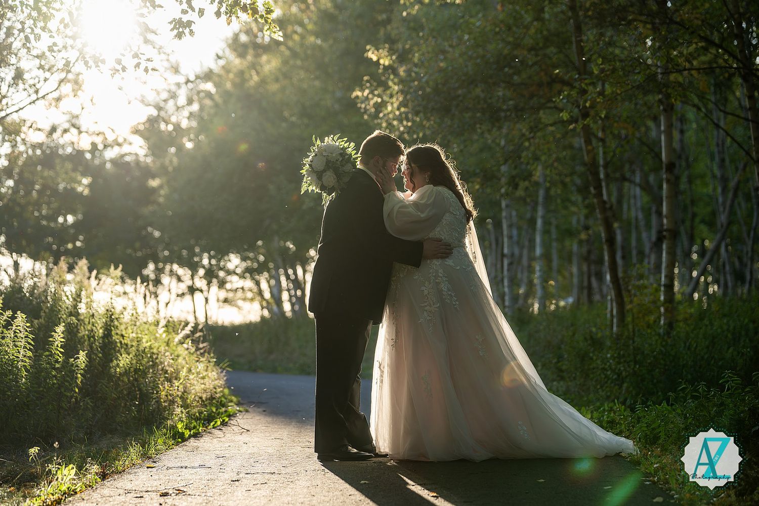 Romantic wedding couple embraces in a sunlit forest path during golden hour.