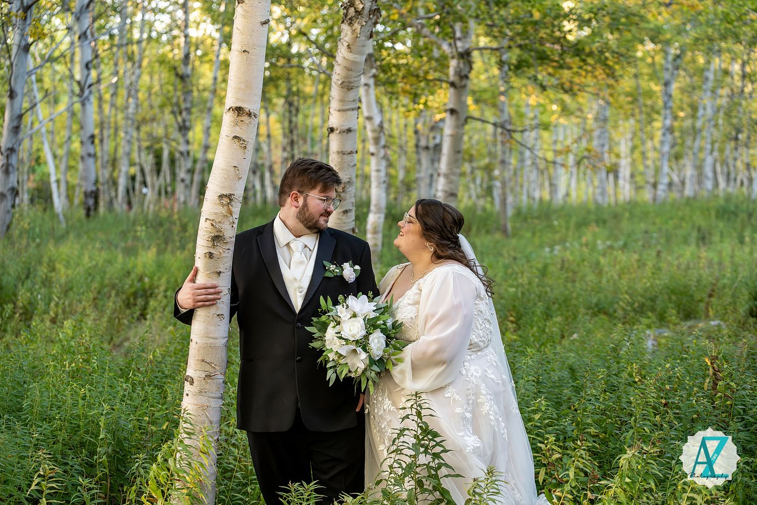 Elegant couple poses among white birch trees in a serene forest setting.