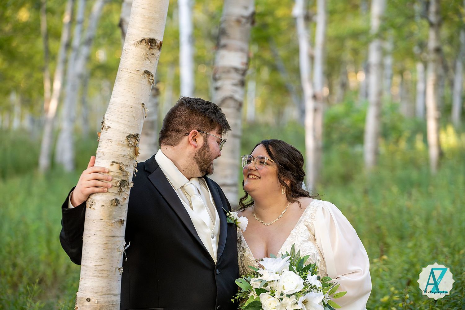 Romantic wedding couple embraces among white birch trees in a sunlit forest setting.