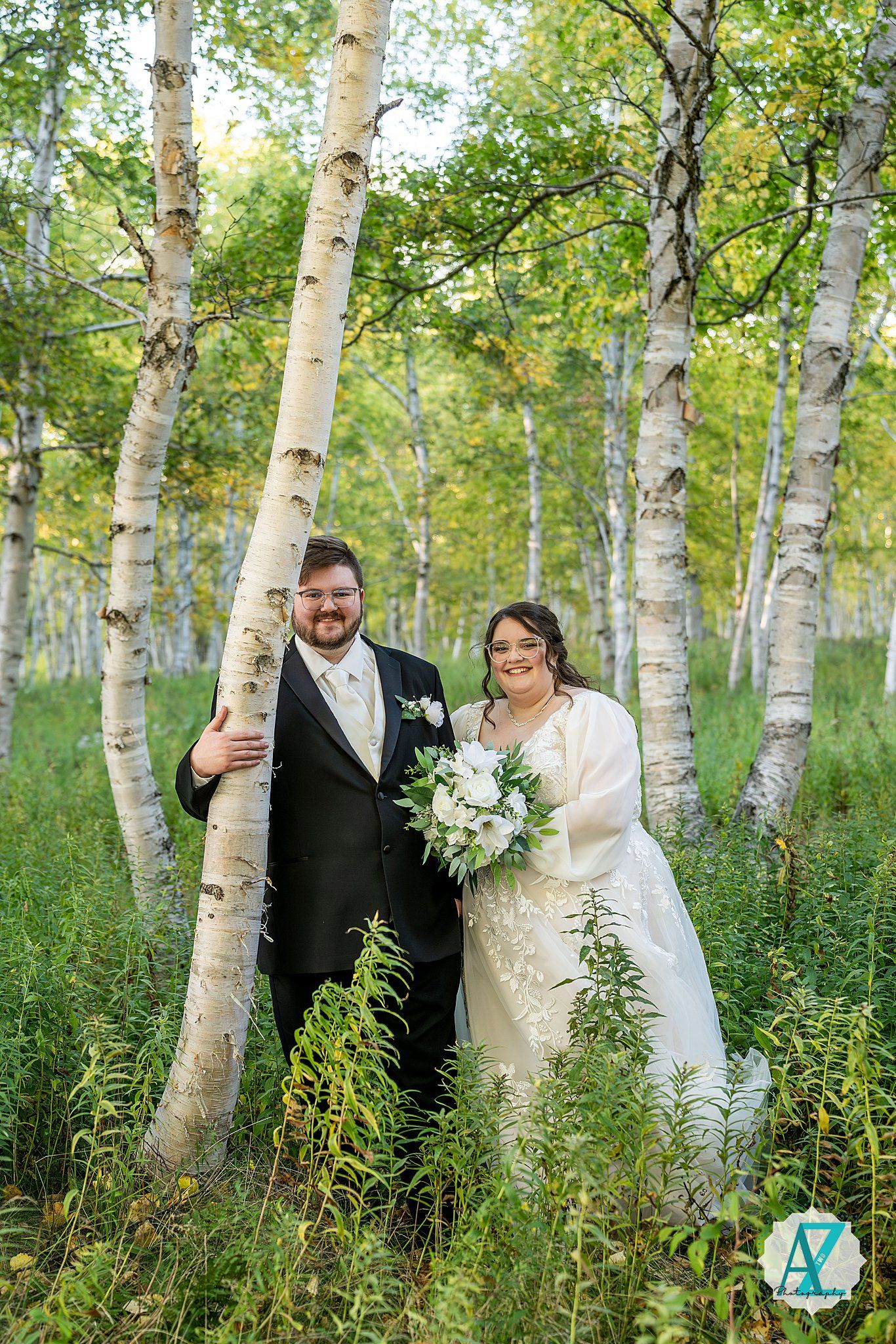 A couple shares intimate moments among white birch trees in a lush green forest setting during their wedding day.