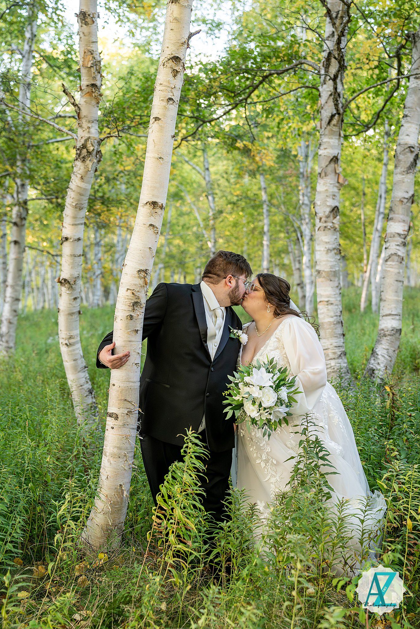 A romantic couple shares an intimate moment among white birch trees in a lush green forest setting.