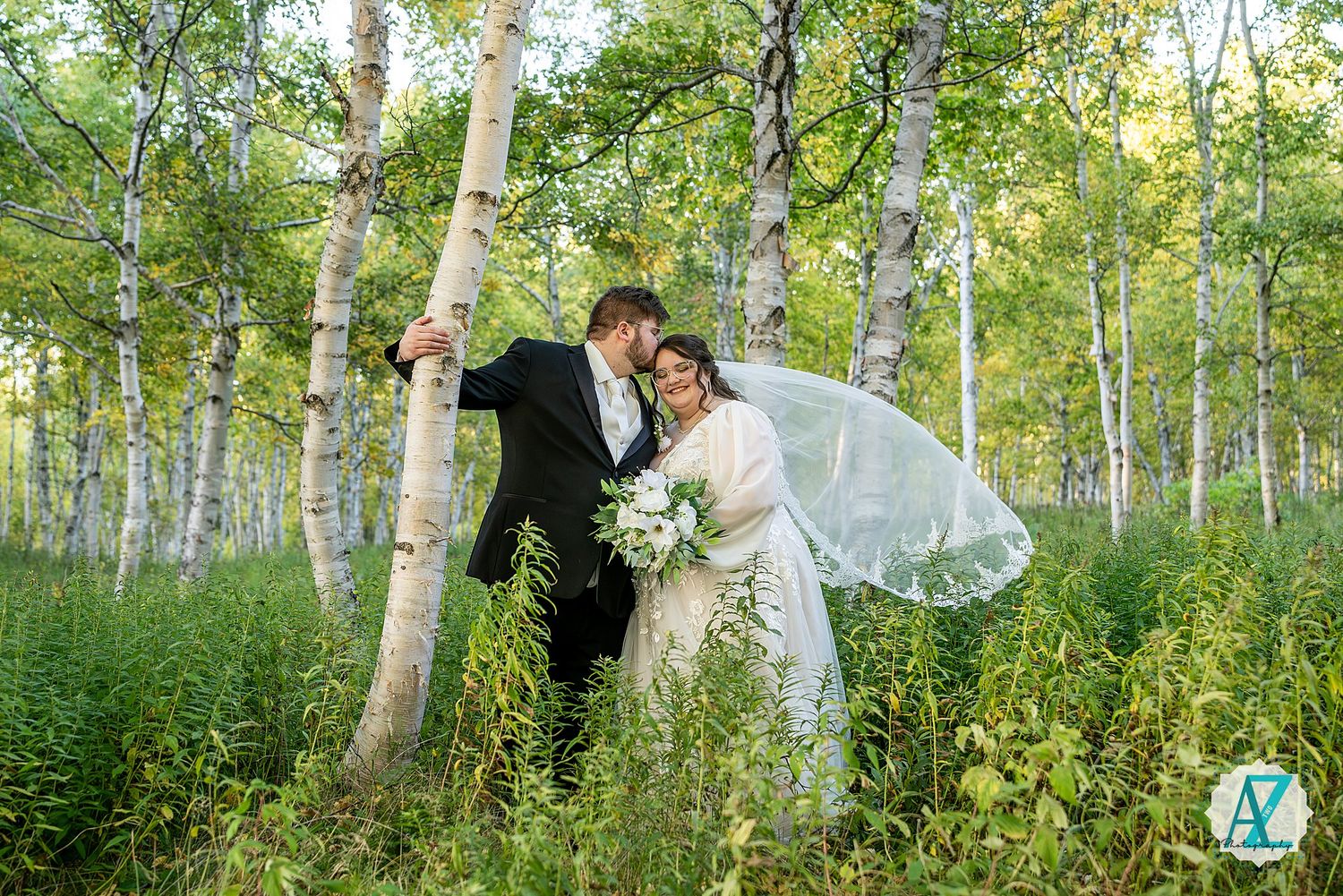 A couple in wedding attire embraces in a serene birch forest with sunlight filtering through the trees.