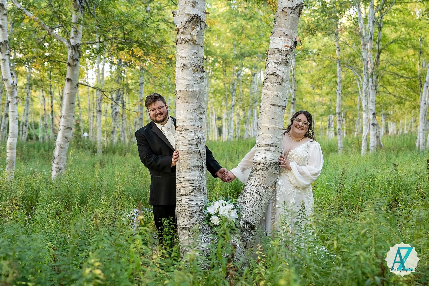 A couple shares a romantic moment among tall birch trees in a lush green forest setting.