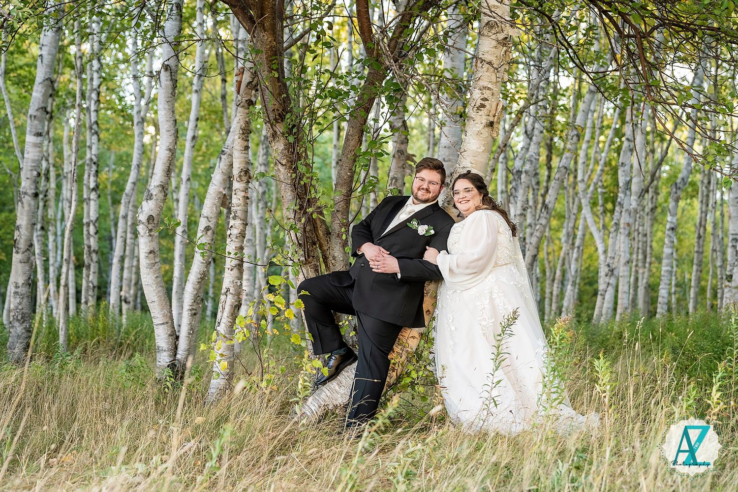Wedding couple poses playfully among white birch trees in a scenic forest grove.