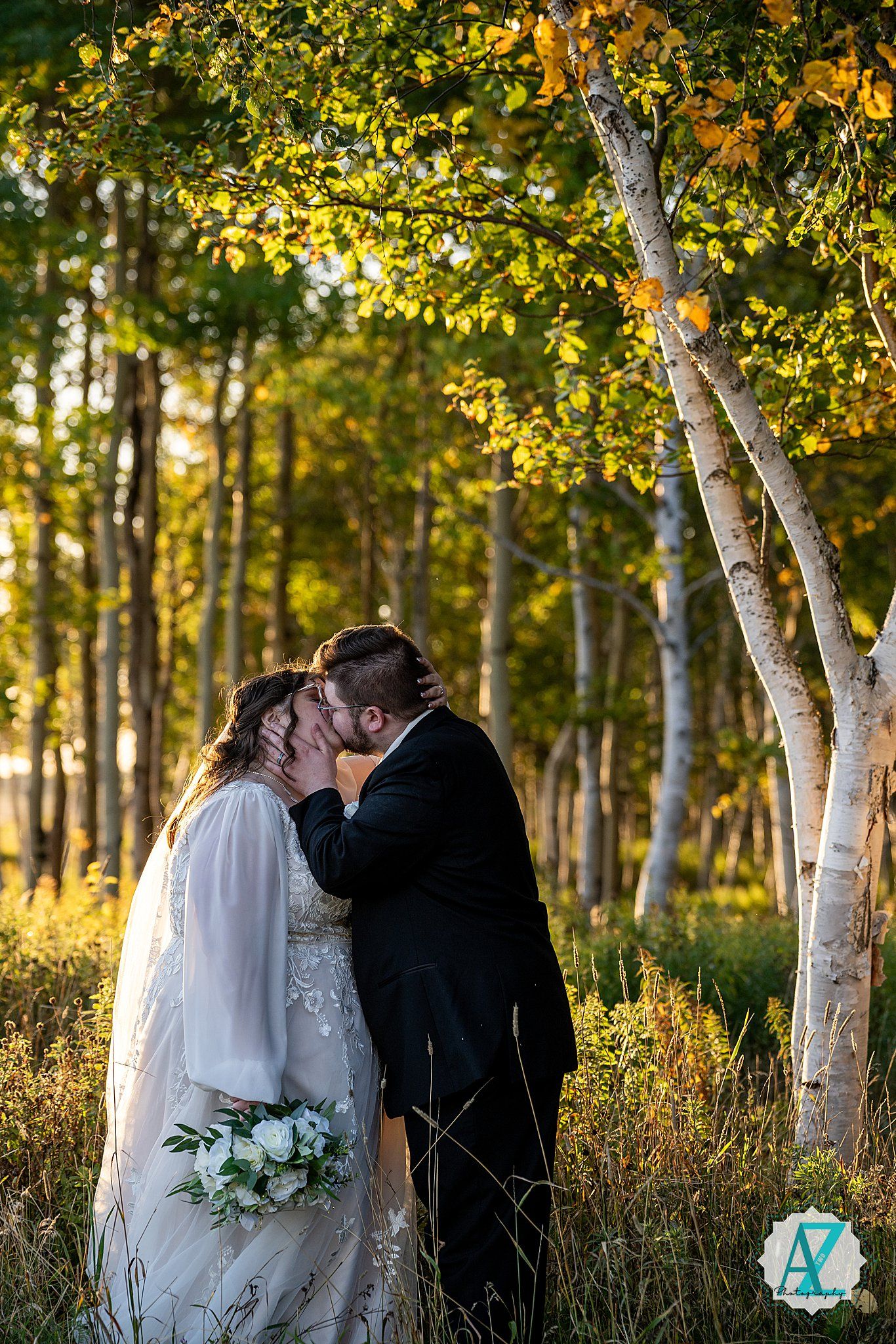 Newlyweds embrace among birch trees at golden hour in a scenic woodland setting.