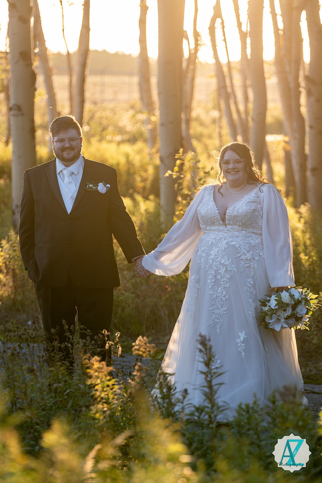 Newlywed couple poses in a sunlit forest with tall trees and golden light filtering through at sunset.