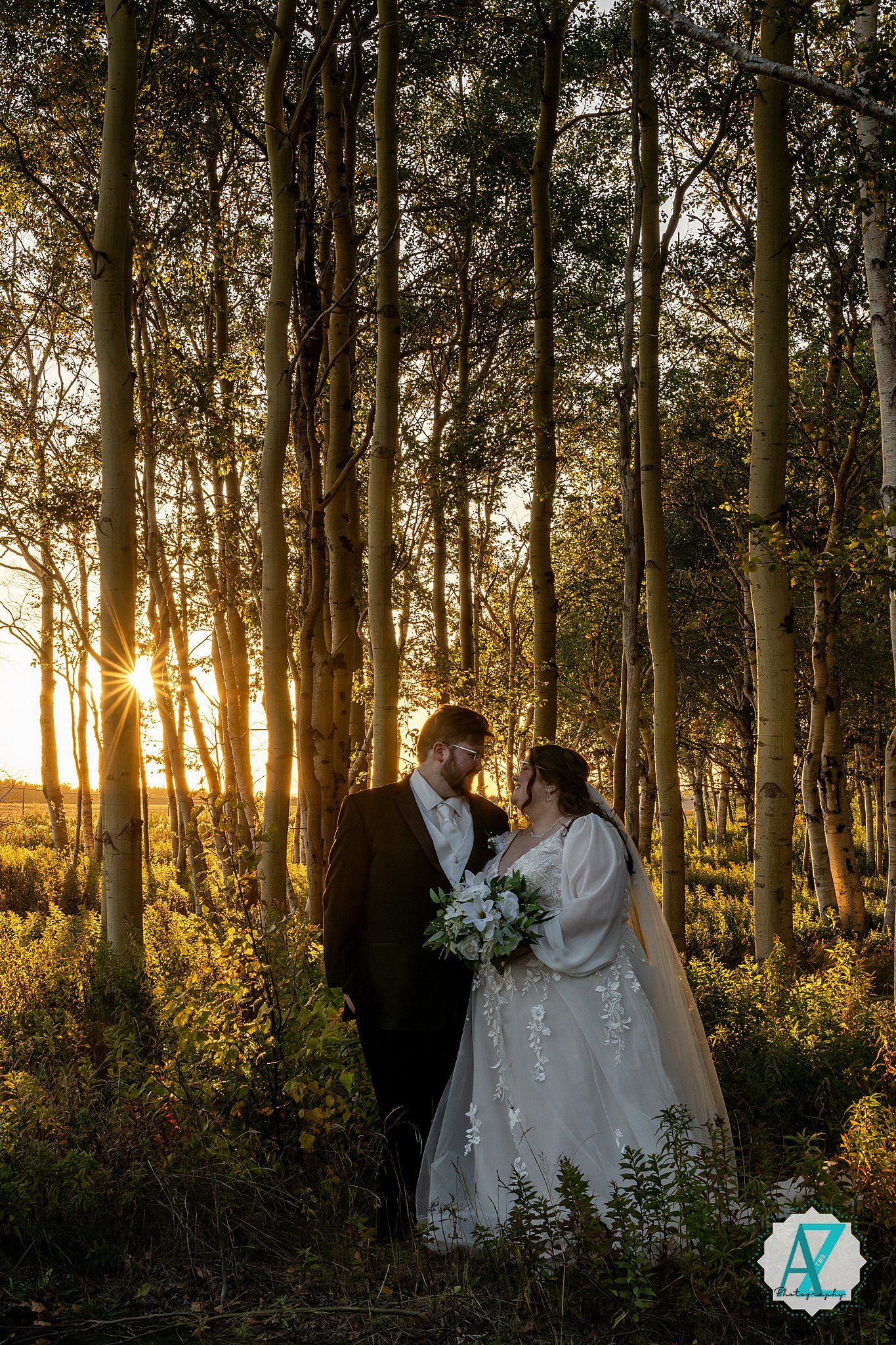 Sunlight streams through birch forest as couple in wedding attire embraces during golden hour.