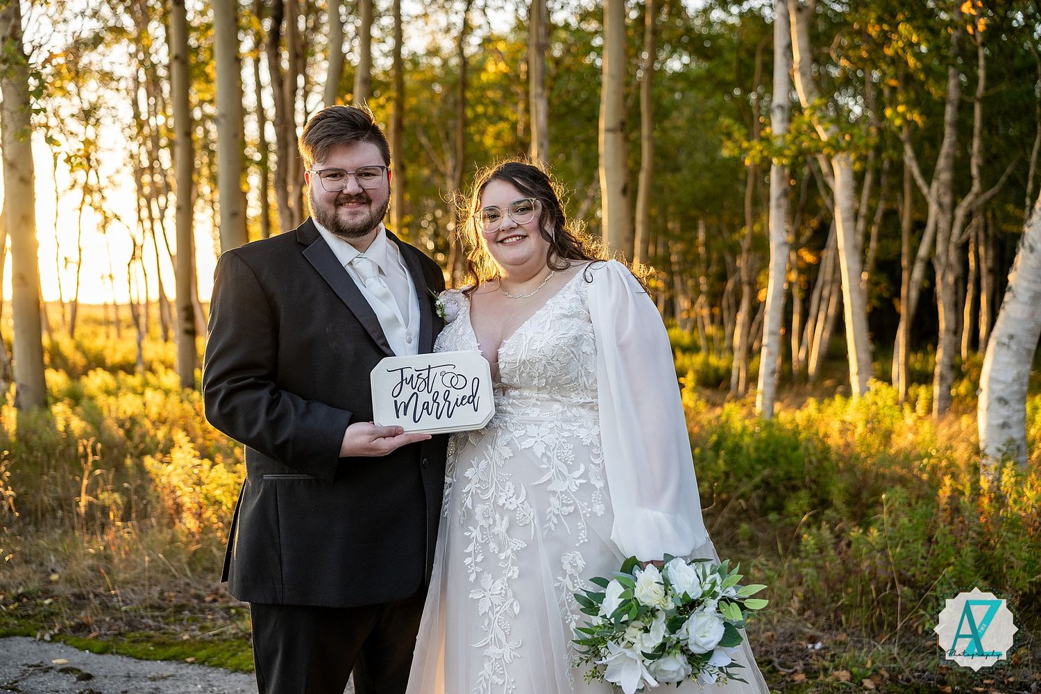 Wedding couple shares a joyful moment together in a sunlit wooded area with autumn foliage.