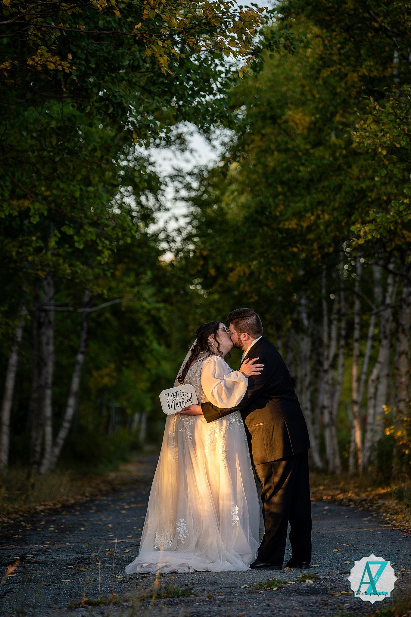 A couple shares an intimate moment on a tree-lined path during their autumn wedding photoshoot.