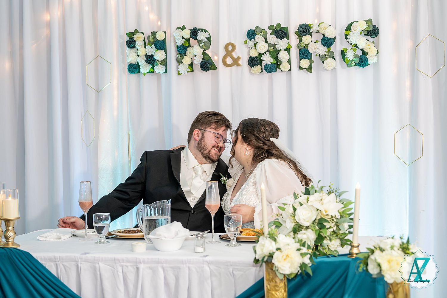 Elegant wedding reception setup with white draping, floral arrangements and romantic lighting at the head table.