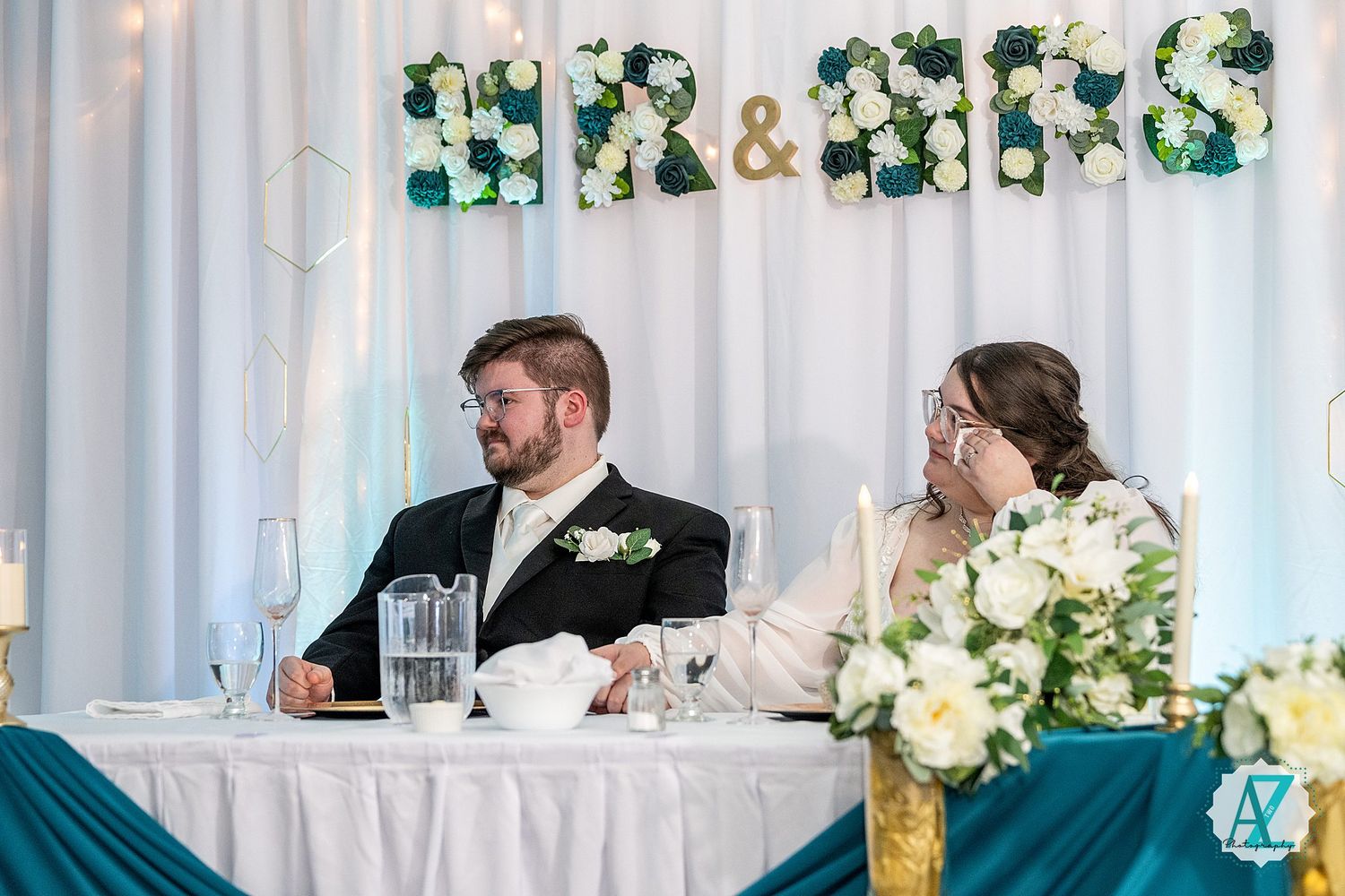 Wedding reception setup with white draping, floral arrangements, and elegant table settings.