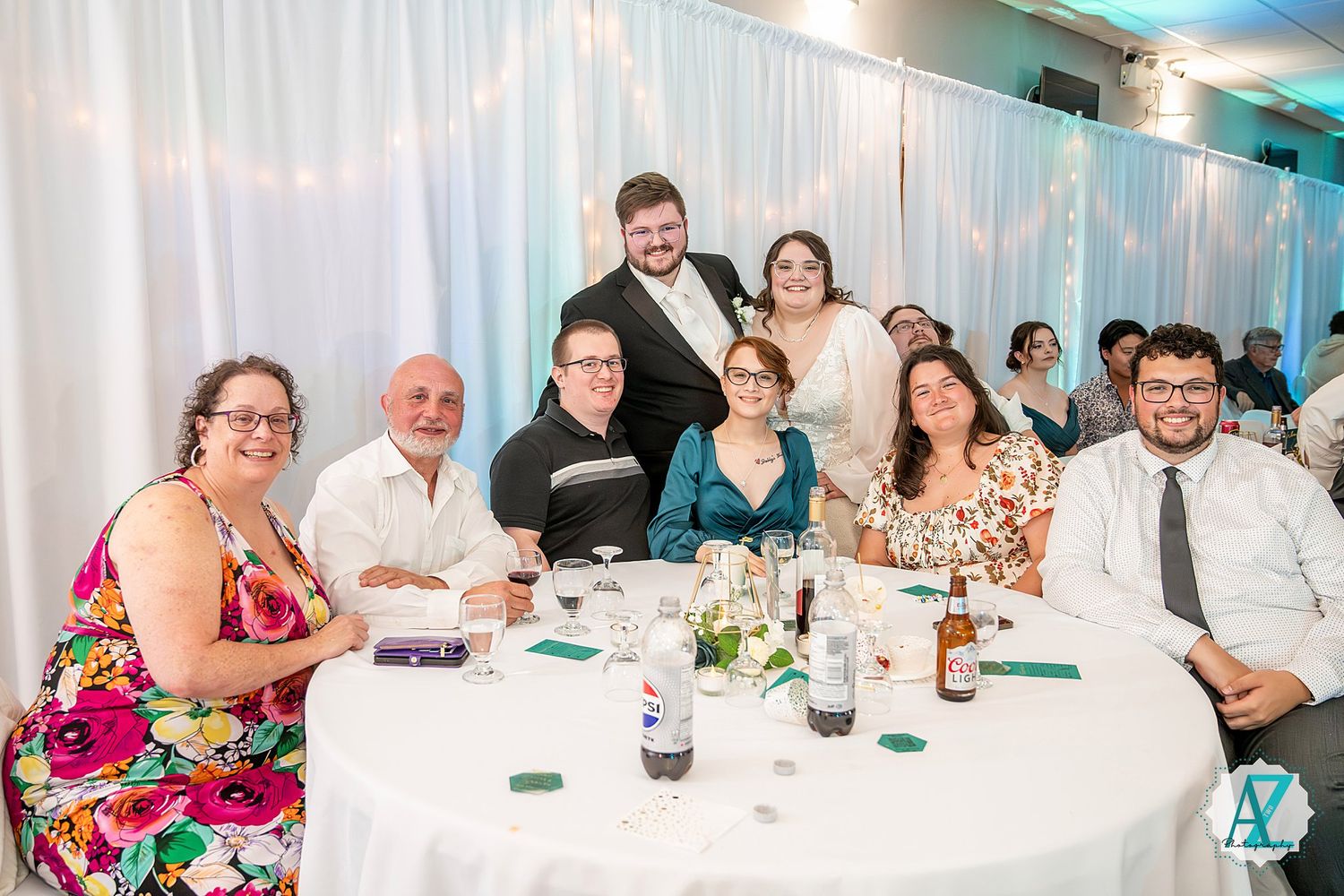 Guests seated at decorated reception tables with white tablecloths and centerpieces in a bright banquet hall.