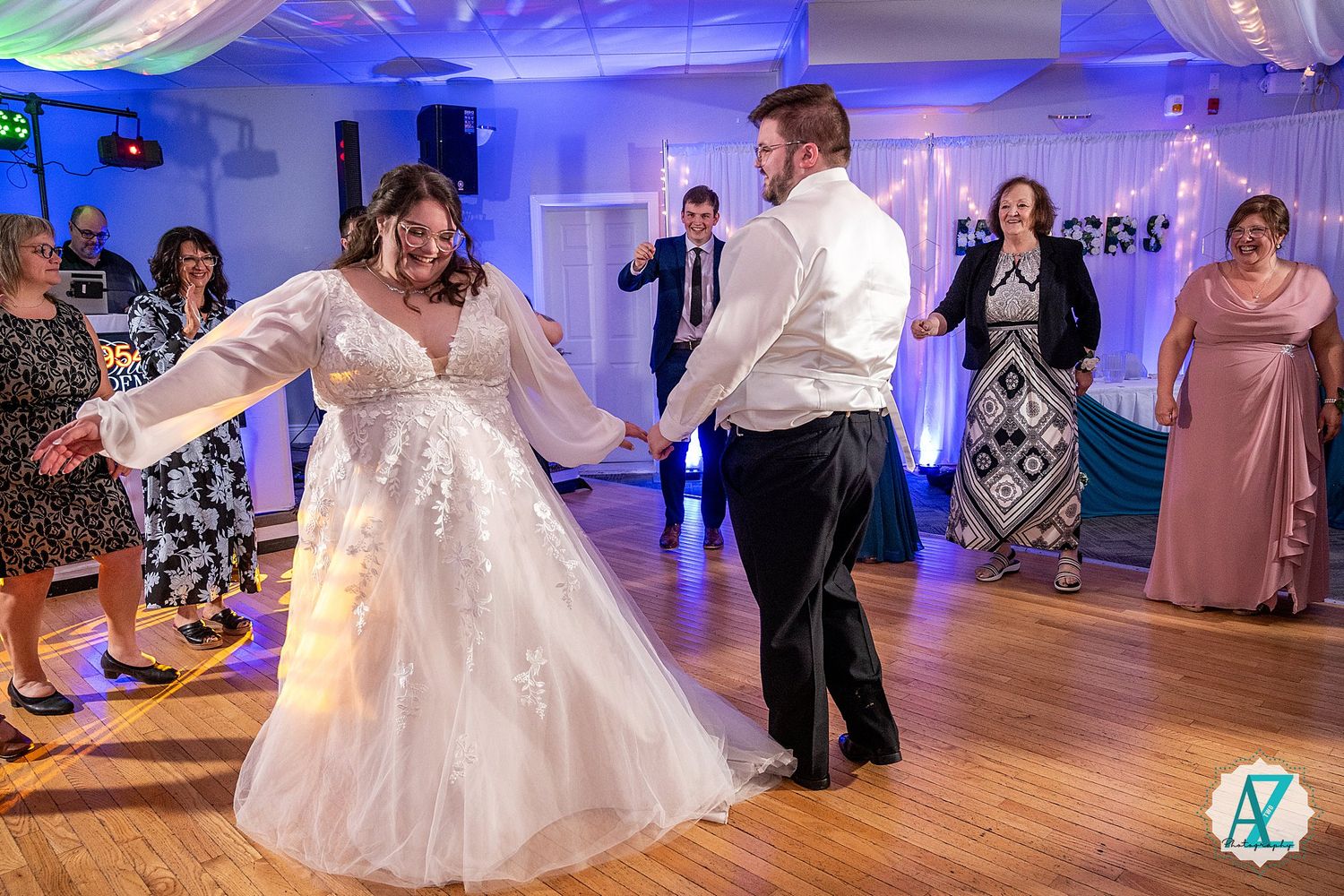 Wedding guests dance together on a ballroom floor illuminated by blue lighting during a reception celebration.