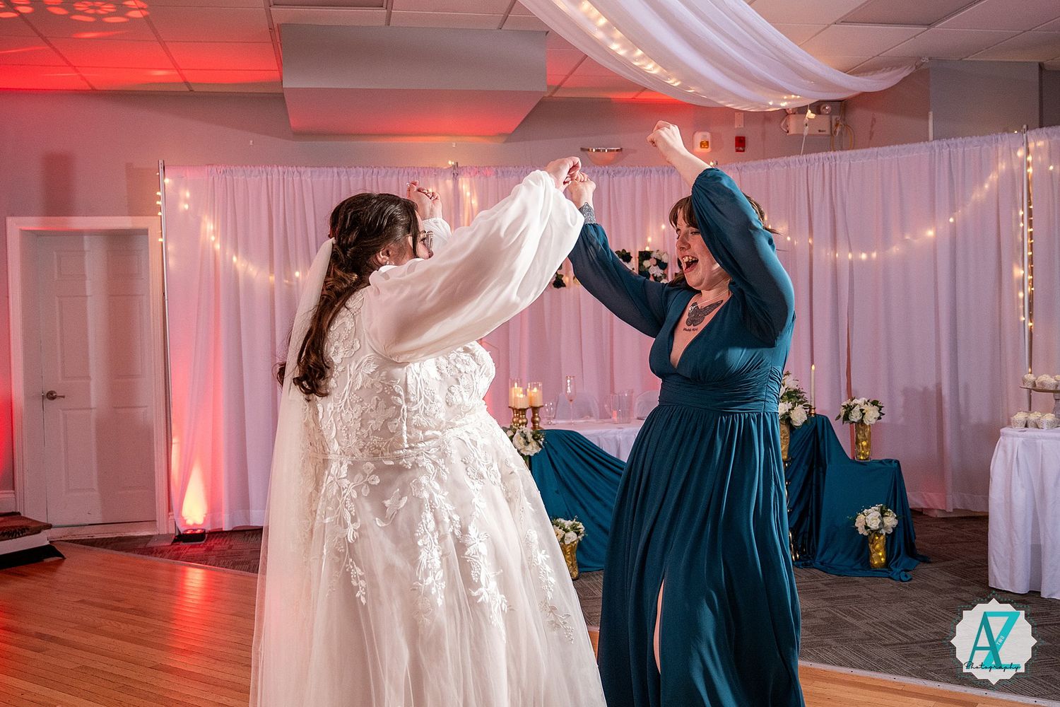 Two people dancing together at a wedding reception with pink lighting and string lights in the background.