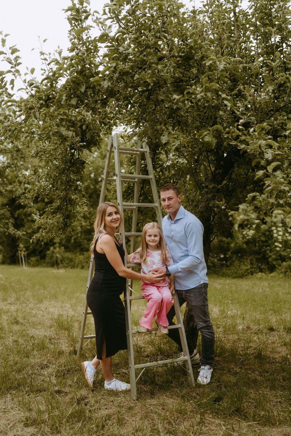 Family enjoying a playful moment together near a wooden ladder in an orchard.