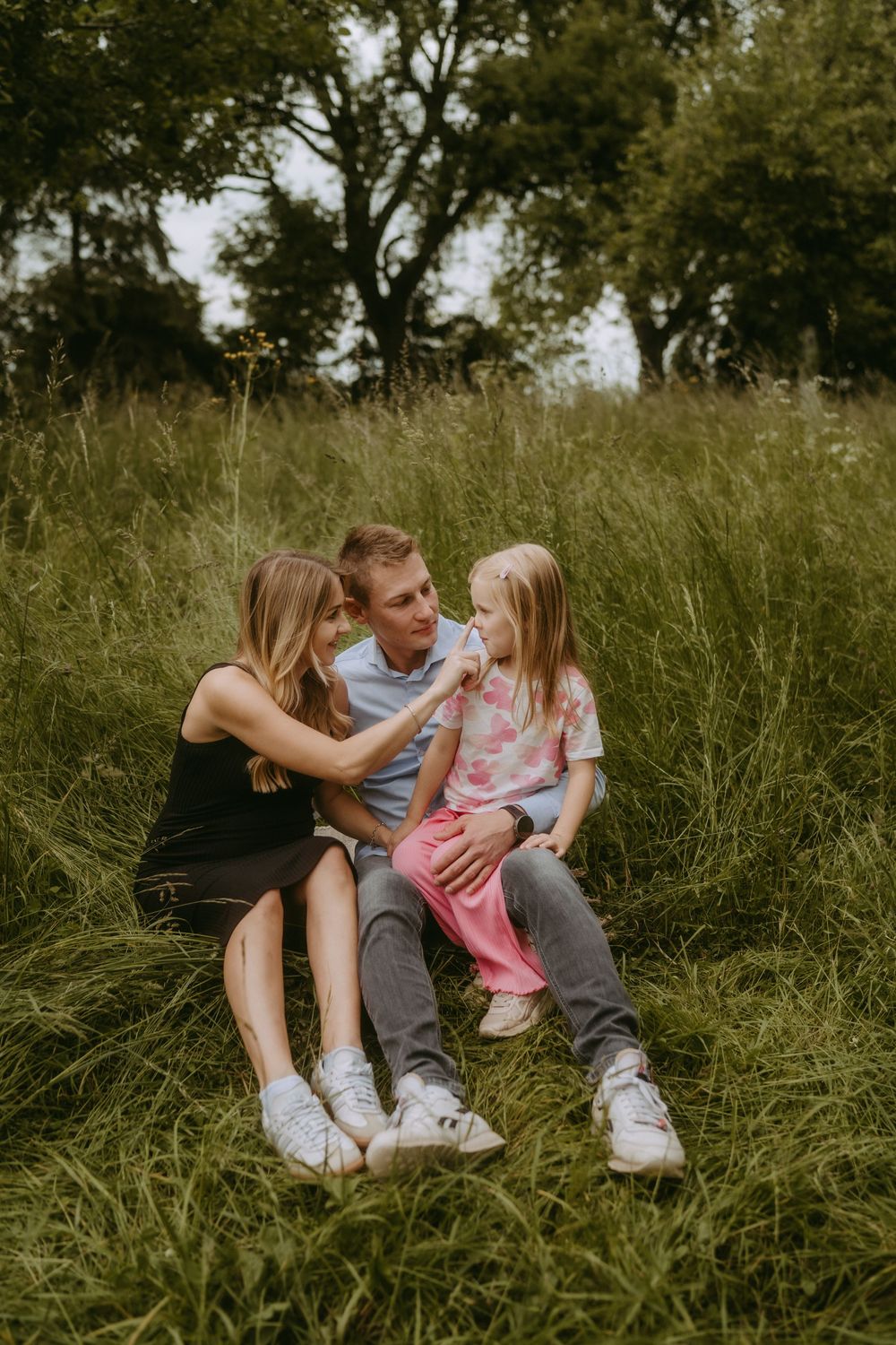 Family sitting close together in long grass during an outdoor photo session.