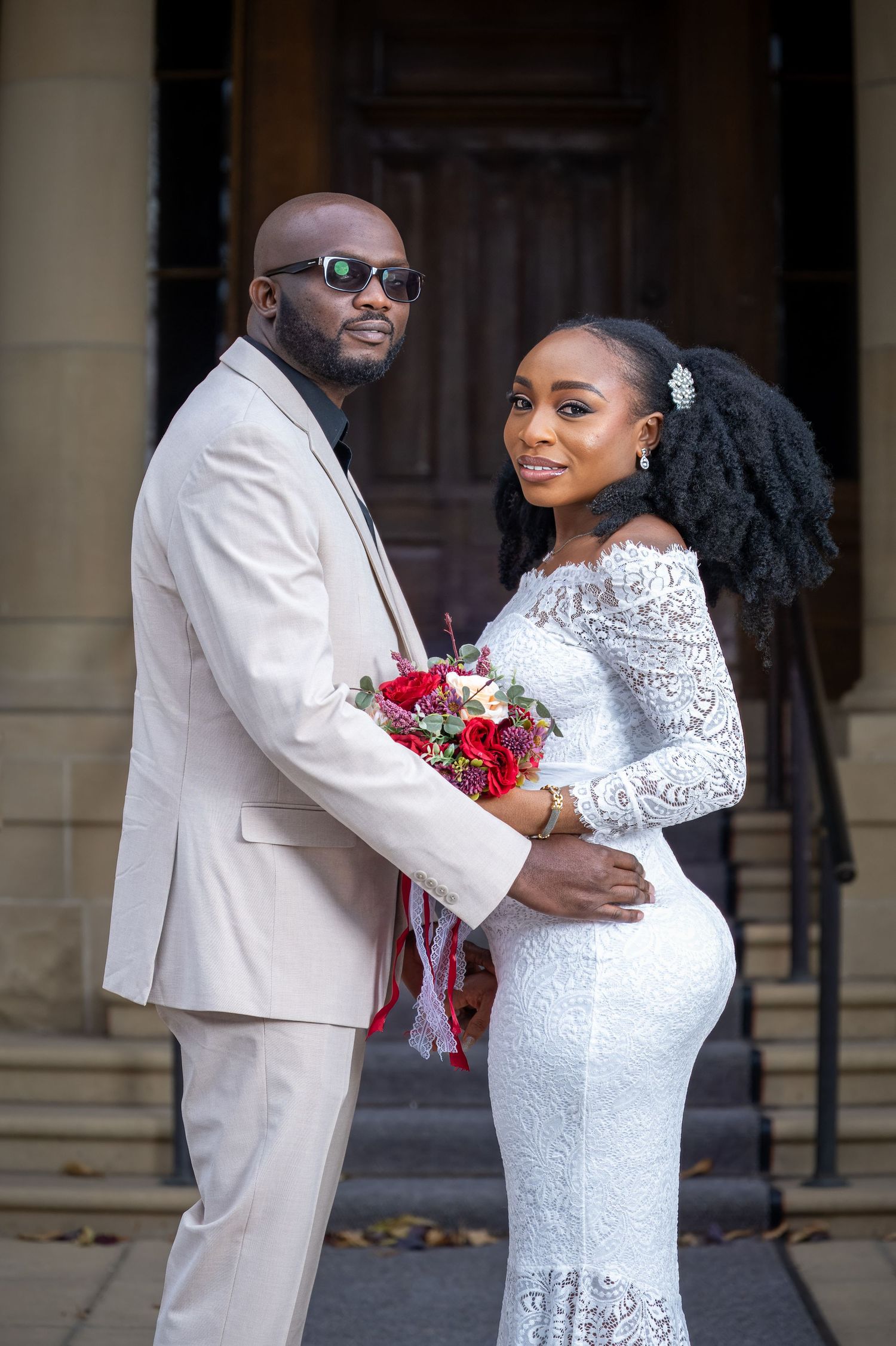 Newlywed couple sharing intimate moments in formal white attire outside historic building.