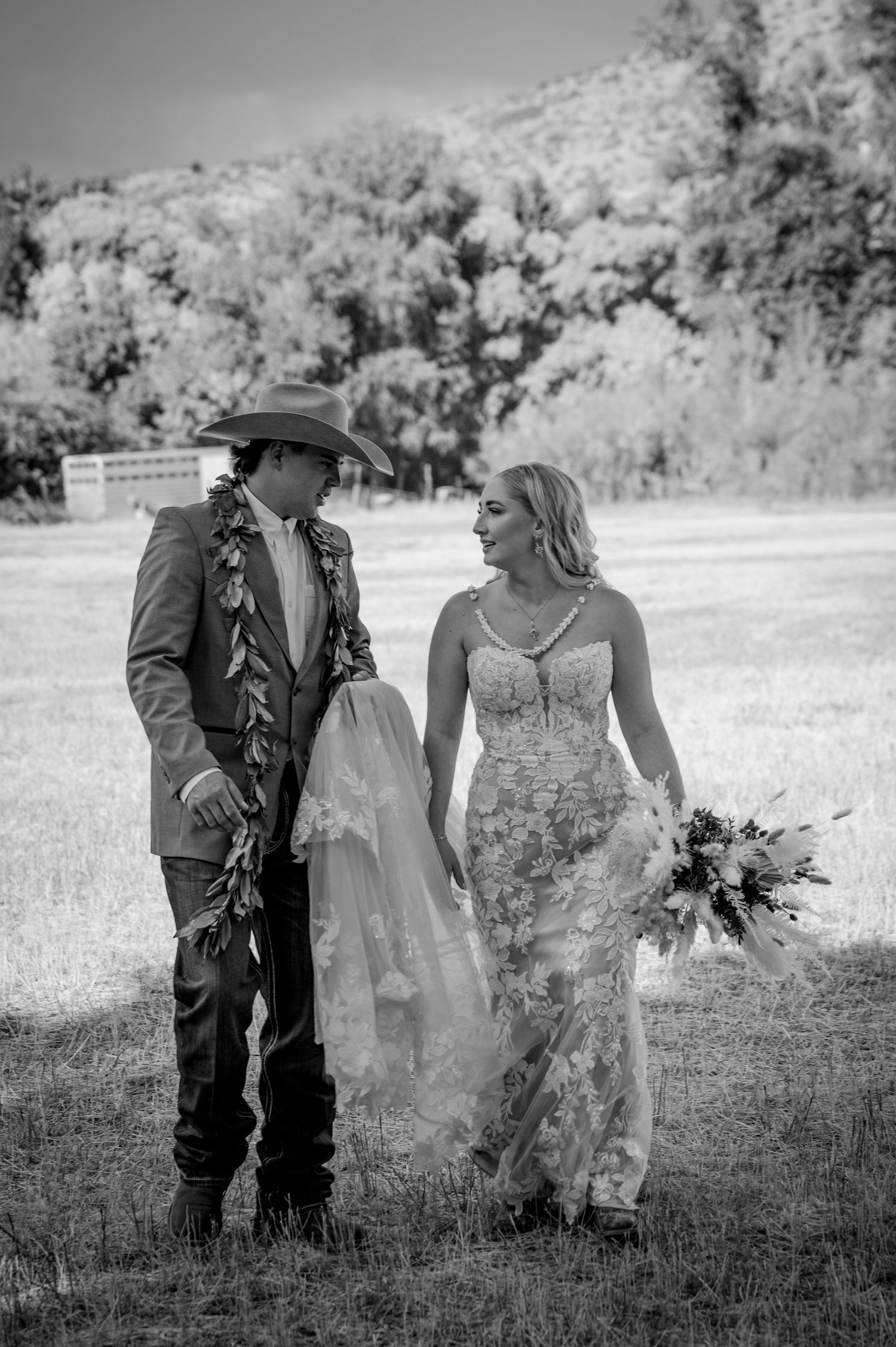 A western-themed wedding couple walks together in a sunny meadow.