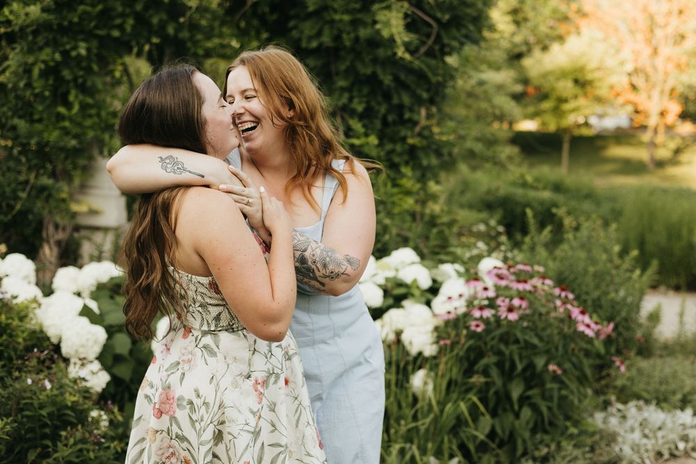 Two people in light colored dresses sit together in a blooming garden during a summer evening.