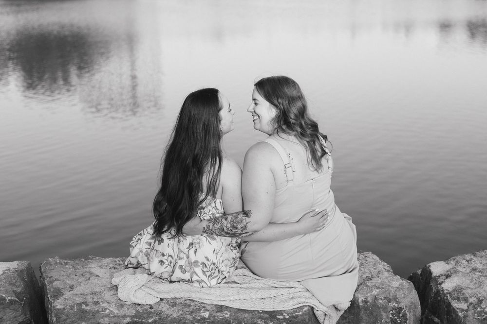 A tranquil waterfront scene with two people sitting close together by a serene lake at dusk in Waterloo Park