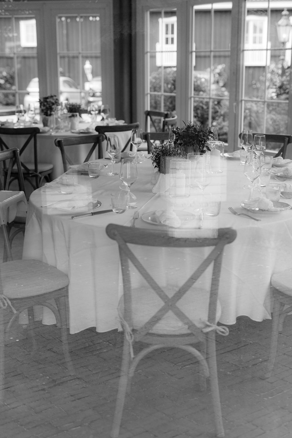 Elegant black and white photo of round dining tables set with white linens and crossback chairs in a restaurant setting.