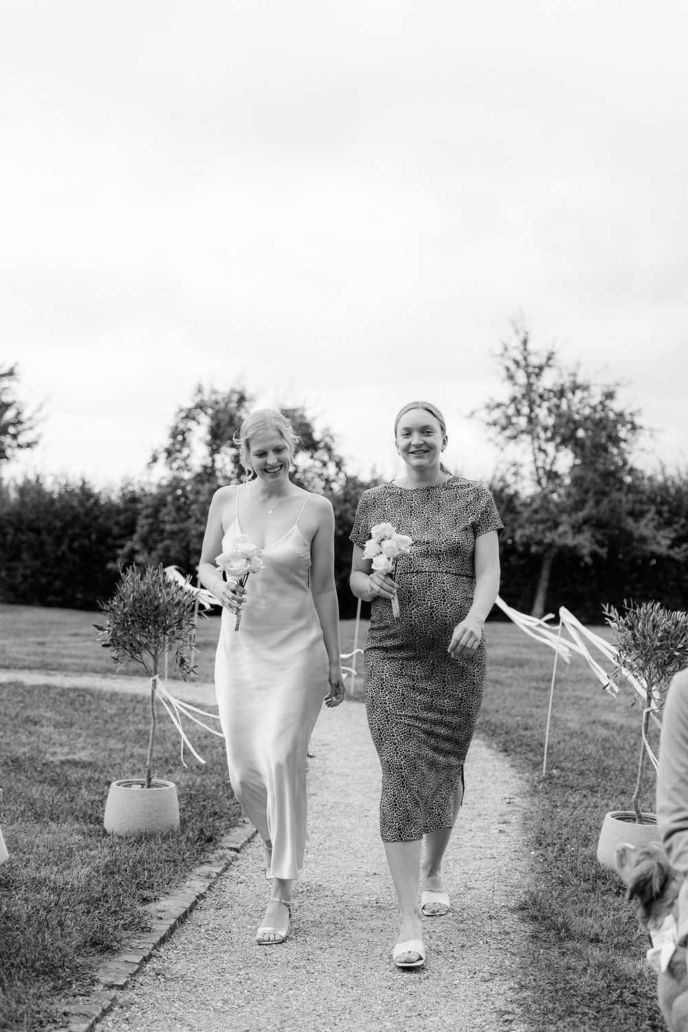 Three people walking together through a grassy field in casual attire on a sunny day.