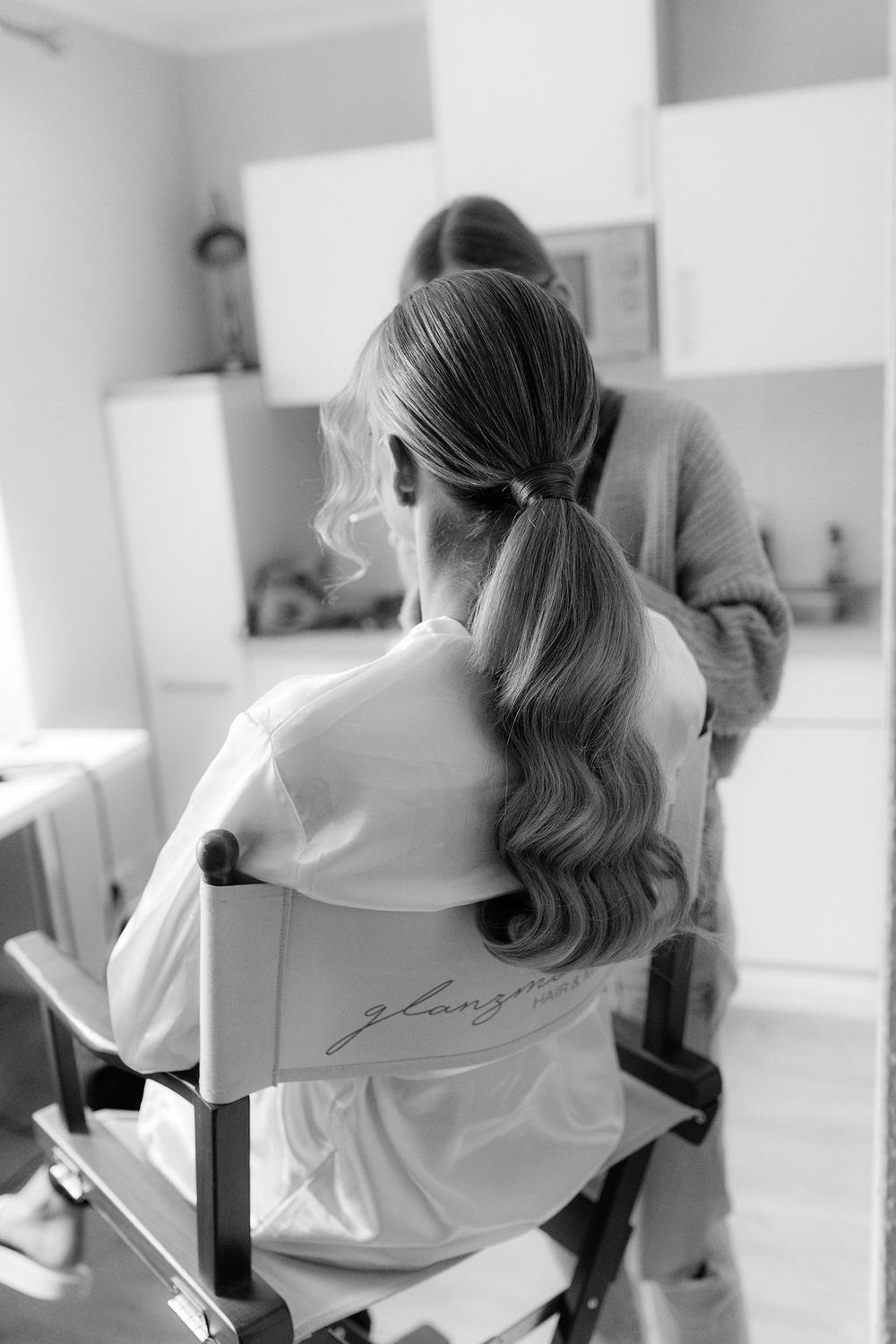 Black and white sequence showing a bride getting her hair styled in an elegant updo for her wedding day.