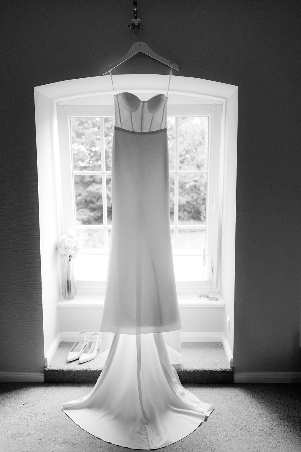 A series of black and white photographs showing a white wedding dress hanging in front of bright windows.