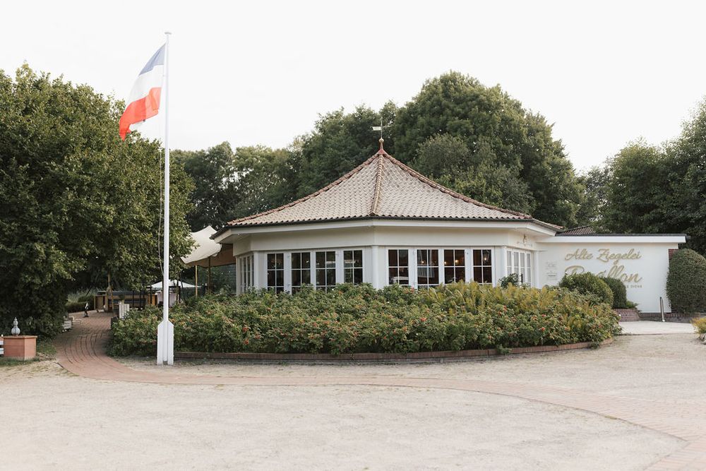 A panoramic view shows multiple white buildings and a flagpole arranged along a curved path at an outdoor facility.