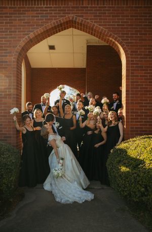 All-black wedding party celebrating outside a historic church, cheering for the newlyweds in joyful excitement – Photography Rhea, LLC