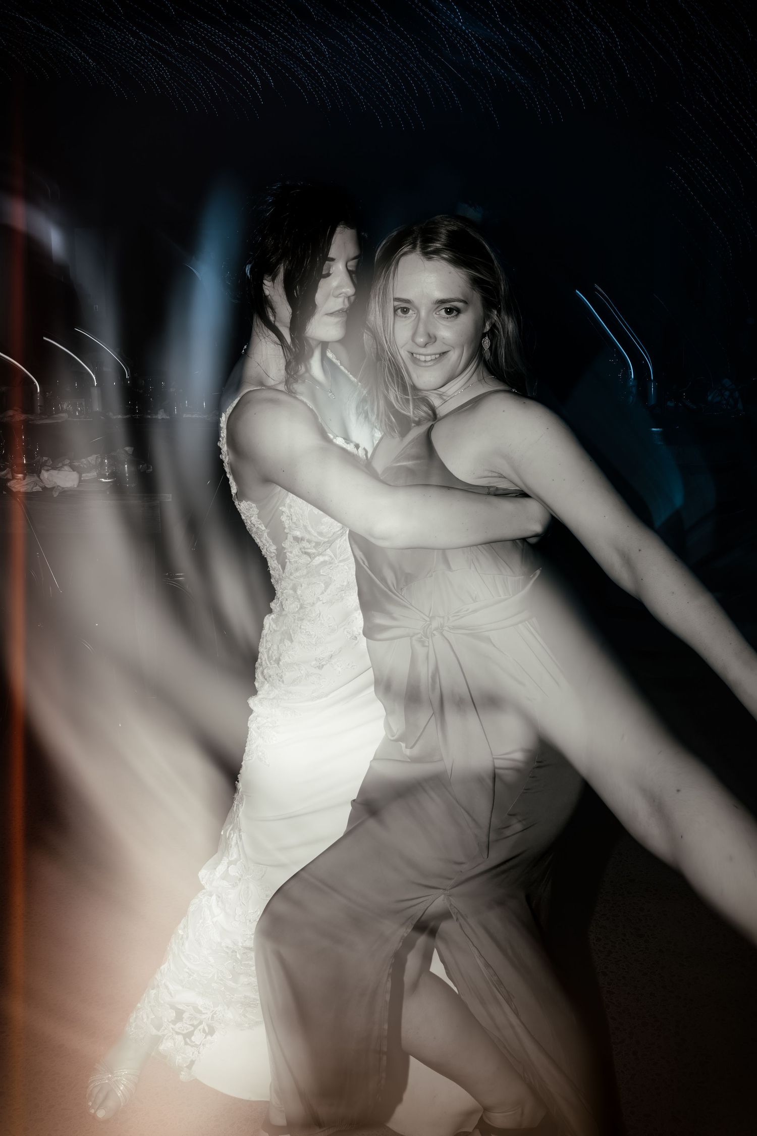 Artistic motion blur photo of people dancing at wedding reception in dark venue.