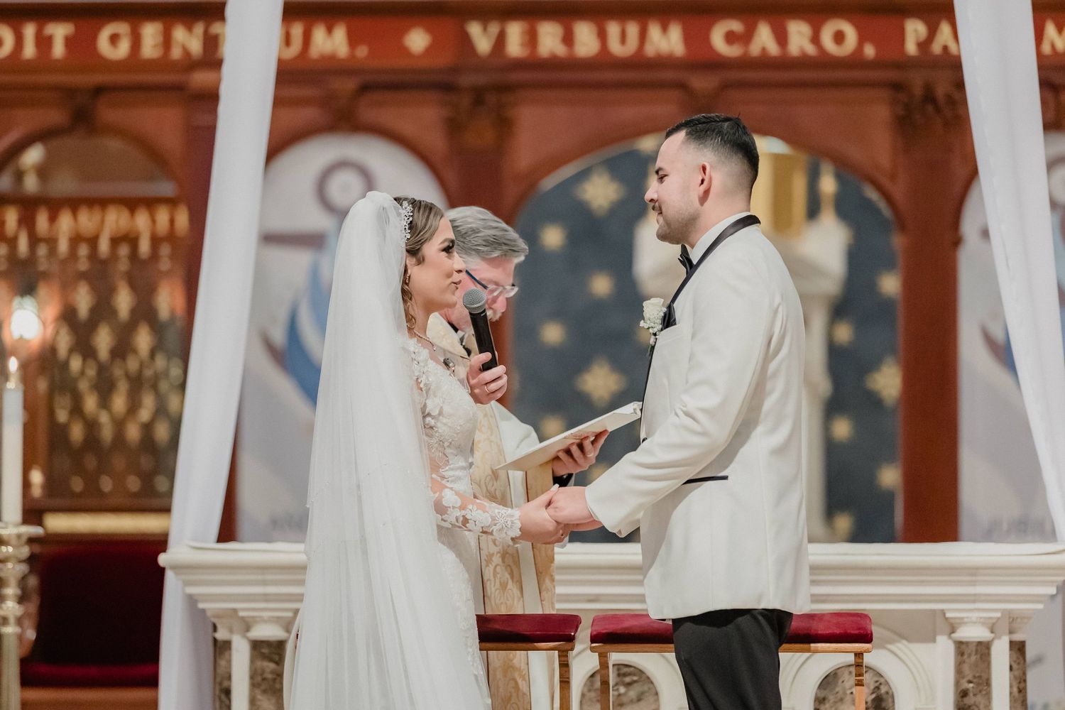 A couple exchanges vows during their wedding ceremony inside an ornate church with decorative red and gold details for Sacramento wedding