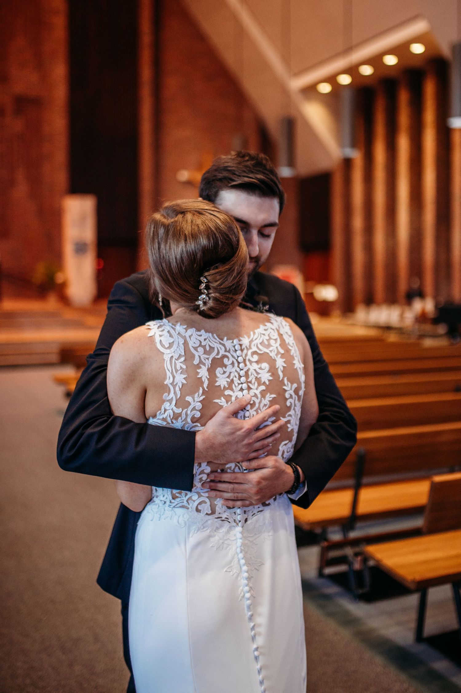 Couple embraces during a first look before their Catholic wedding ceremony in church with elegant lace back dress and dark suit.