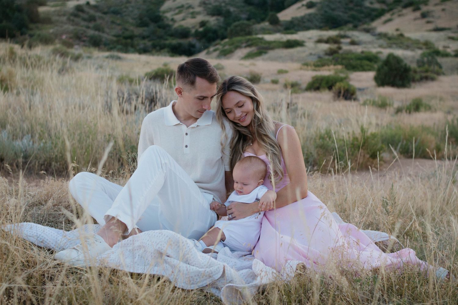 A couple in white and pink outfits reclines together in a rustic outdoor field setting.