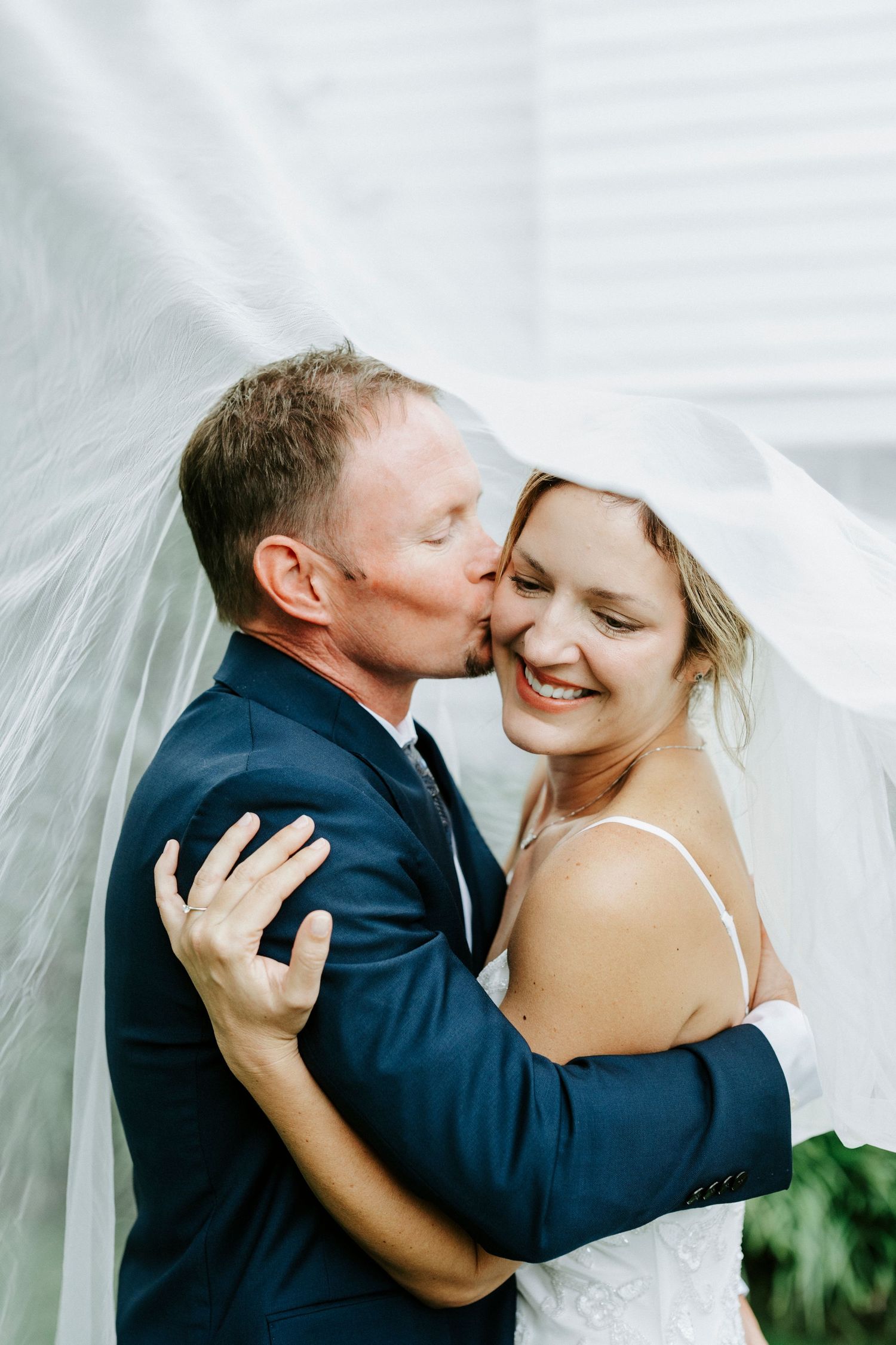 A romantic wedding moment captured through a veil as a couple shares an intimate embrace and kiss.