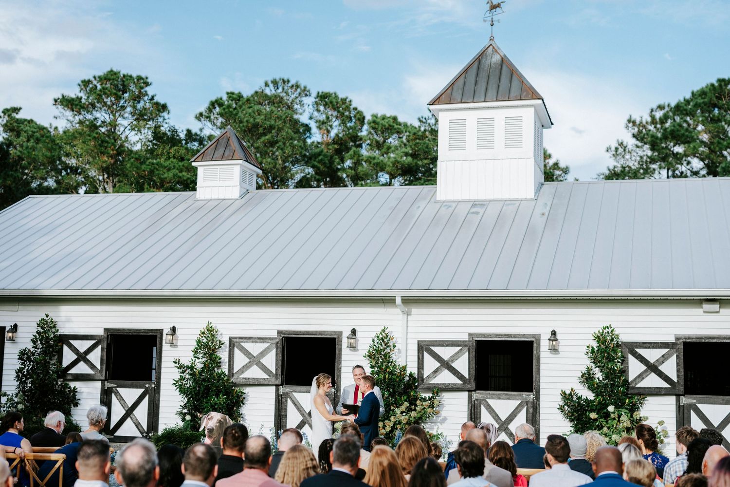 A large outdoor wedding reception under a white tent with guests mingling and dining at decorated tables.