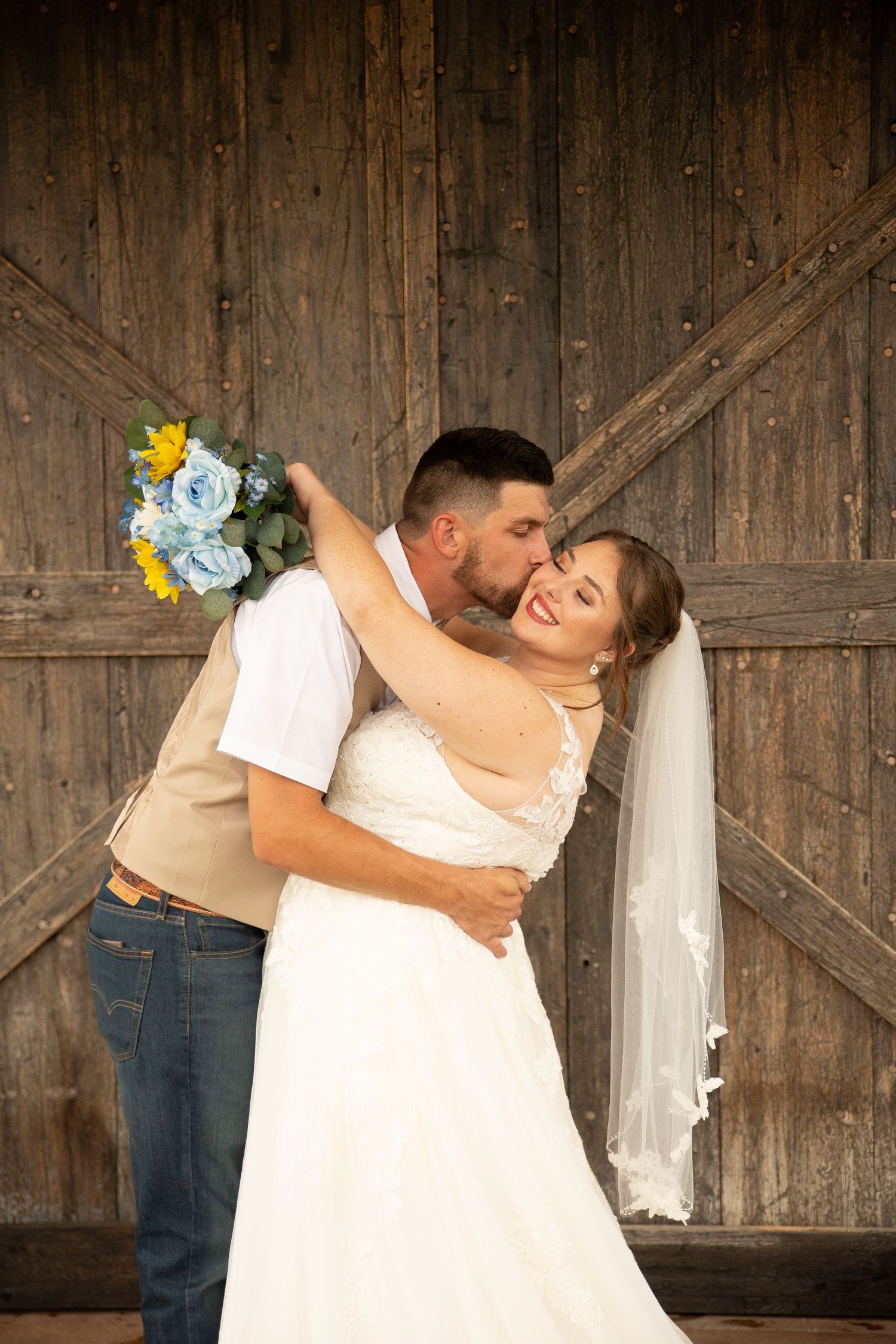 A couple in wedding attire shares romantic dance poses against a rustic wooden barn door backdrop.