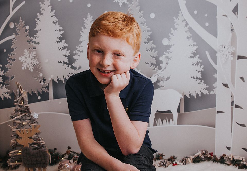Child sitting against winter wonderland backdrop with snowflake decorations and white trees.