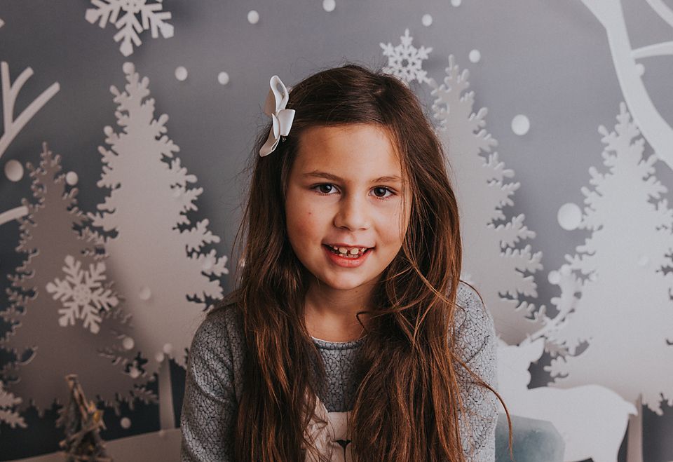 Young person poses against winter-themed backdrop with snowflakes and white forest silhouettes.