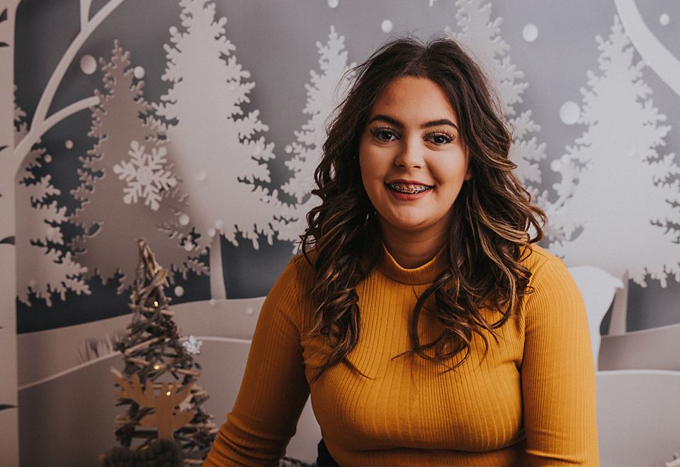 Woman in yellow turtleneck sweater smiles warmly against winter forest backdrop.