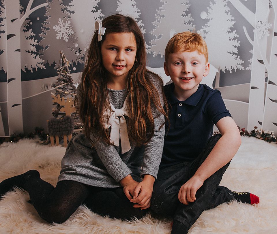 Children and adults pose together on a white floor against a winter forest backdrop with snowflakes.