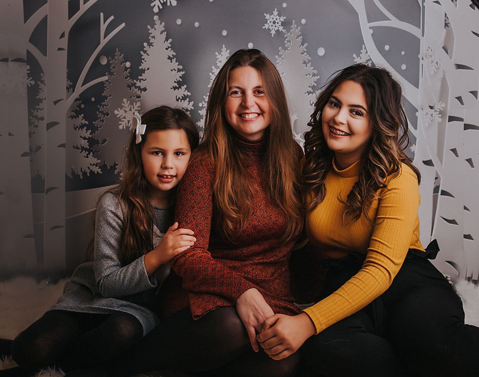 A group sits together against a winter-themed backdrop with birch trees and snowflakes for holiday photos.