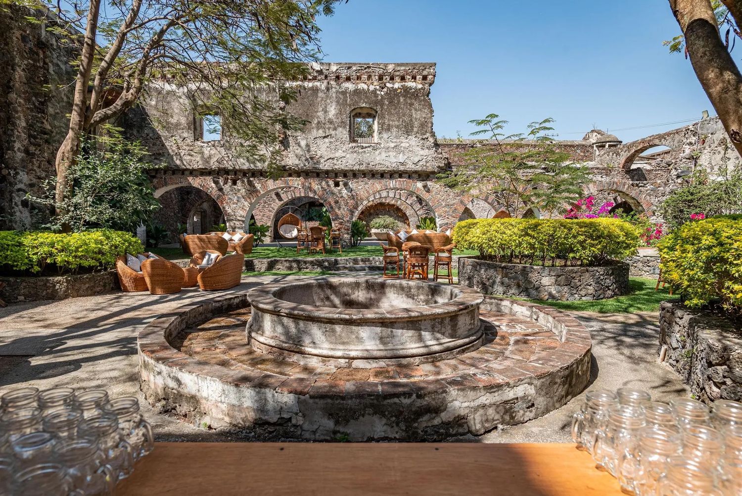 Rustic stone courtyard with decorative fountain and tropical plants under bright blue sky.